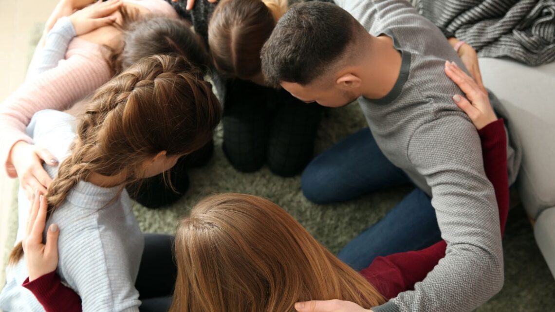 A group of young people hugging each other and praying